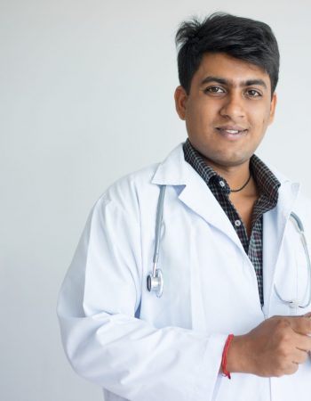 Friendly Indian doctor reviewing medical history on tablet. Smiling young practitioner holding device and posing at camera. Digital technology in medicine concept